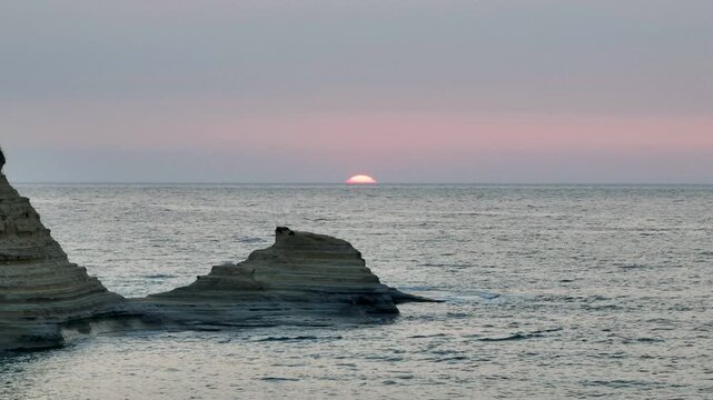 Close-up aerial drone shot of the sun setting on the horizon, framed by the iconic layered rock formations of Canal d'Amour in Sidari, Corfu