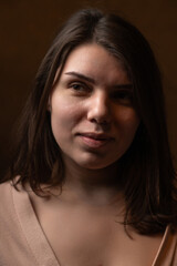 Fototapeta premium Female model with long dark hair wearing a beige wrap top poses confidently against a dark backdrop, showcasing a soft lighting effect and elegant posture