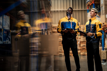 Obraz premium Creative reflection of diverse factory supervisors working in storehouse aisle. Industrial logistics teamwork managing safe cargo distribution using smart tablet.