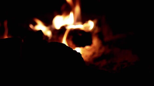 Blurred shot of a bonfire burning brightly at night. The flames create a warm glow, and the blurred foreground adds a sense of depth and mystery. Suitable for projects about camping, nature.