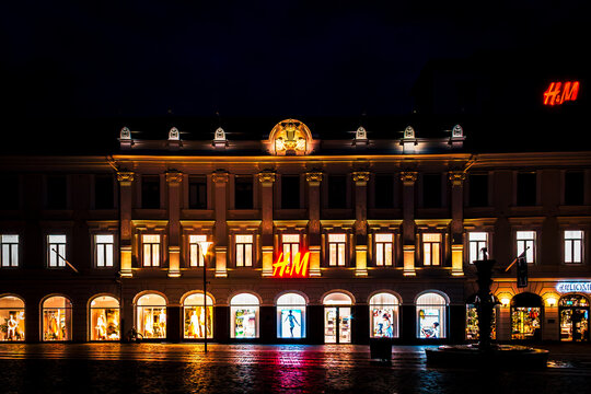 Malm&ouml;, Swden - May 20 2019: lluminated historic building facade with a fashion retail store HM neon sign and colorful light reflections on a wet cobblestone square at night