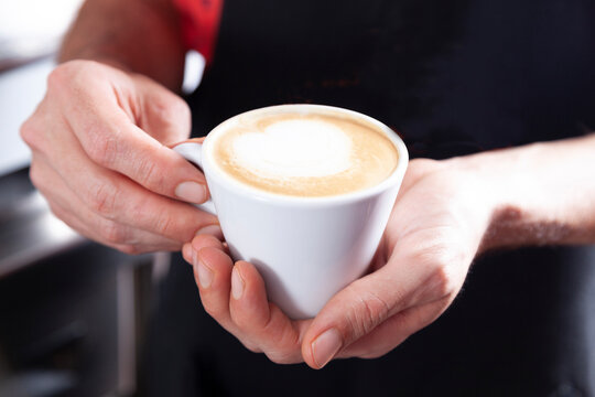 Hands holding a cup of coffee with milk in a caf&eacute;.