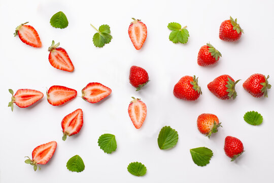 Strawberries, halved strawberries, and leaves on a white background.