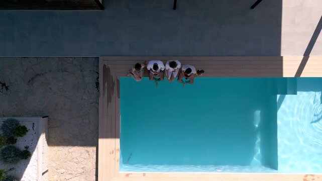 Aerial view of adult friends relaxing next to outdoor pool during summer vacation.