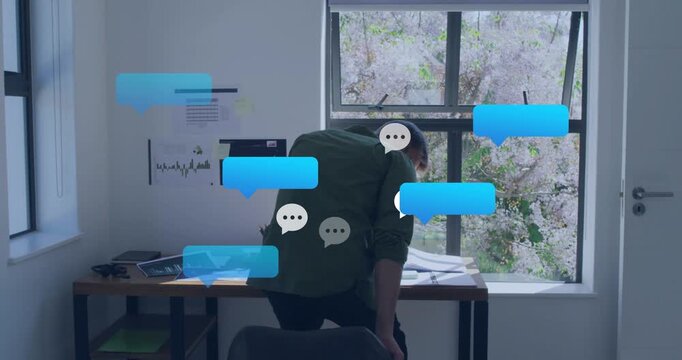 Man at desk sitting after blue chat bubble popping, answering phone and working laptop for business