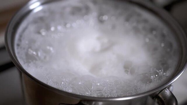 Water boils vigorously in a pot on a stove, creating a swirling pattern of bubbles and foam. Ideal for cooking shows and food blogs.