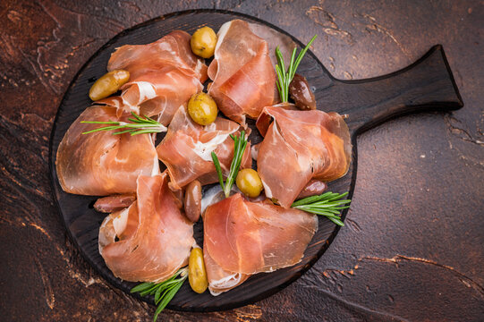 Gourmet Italian Prosciutto with fresh rosemary on a dark round plate.
