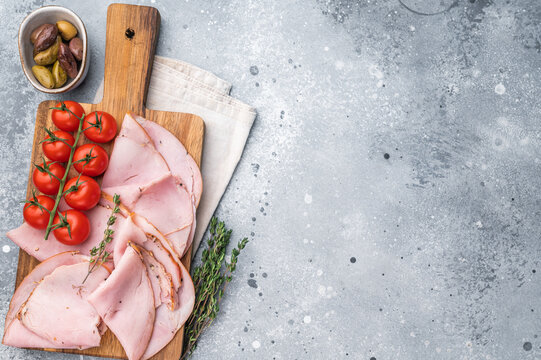 Sliced Prosciutto cured pork, cherry tomatoes and thyme displayed on a wooden cutting board with a light napkin on a textured gray backdrop.