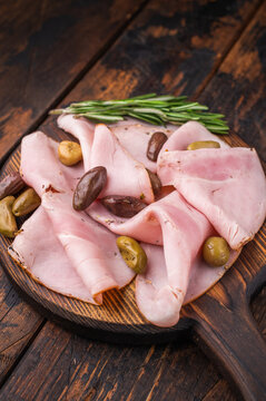 Cured pork slices lonza with olives and rosemary on a rustic wooden board over dark aged wood creating a simple and commercial food background.