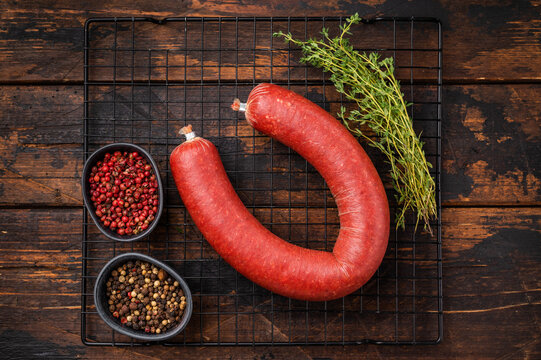 Whole raw Turkish sucuk (sujuk) on a cooling rack with thyme. Spicy dry-cured sausage on a rustic wooden background.