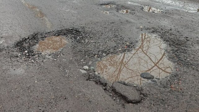 Puddle in broken road with deep pothole after rain 