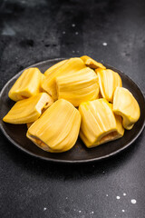 Sweet, golden yellow jackfruit pods (bulbs) served in a black plate on a dark stone background. Exotic tropical fruit with copy space © Mironov