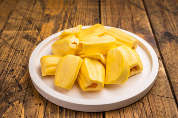 Sweet, golden yellow jackfruit pods (bulbs) served on a white plate on a rustic wooden table. Fresh, tropical fruit snack. © Mironov