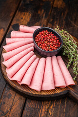 Gourmet charcuterie board featuring fan folded bologna/mortadella, pink peppercorns, and fresh thyme on dark wood. © Mironov