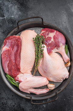 Raw duck parts breast wing thigh and fillet with herbs and garlic in metal pan on dark stone background with fork ideal for poultry stock images.