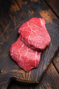 Marbled Wagyu beef chuck resembling angus and yakiniku cuts arranged with thyme and garlic on dark wood background great for food photography.