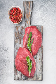 Uncooked Wagyu top blade chuck steaks with deep texture served on aged wood with herbs and pepper on pale gray background perfect for butcher and culinary stock.