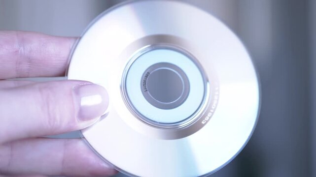 A hand holds a CD against a blurred background. Light shines through, revealing the disc's structure and data.