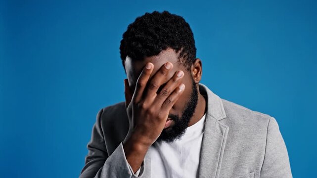 Man with hand on face expressing frustration against a blue background