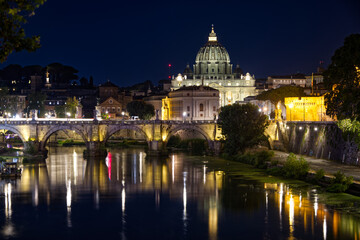 Fototapeta premium Spectacular nighttime view of St. Peter's Basilica rising above the Tiber River in Rome, Italy. The illuminated dome, historic bridges, and shimmering reflections create a timeless cityscape highlight