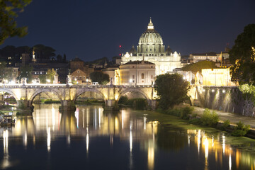 Fototapeta premium Spectacular nighttime view of St. Peter's Basilica rising above the Tiber River in Rome, Italy. The illuminated dome, historic bridges, and shimmering reflections create a timeless cityscape highlight