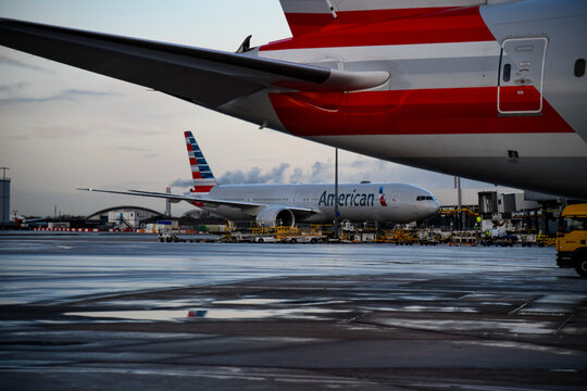 Illustrative editorial-style image of an American Airlines Boeing 777 parked at a gate at London Heathrow Airport (LHR) with another American Airlines aircraft in the background. Ideal for aviation, c