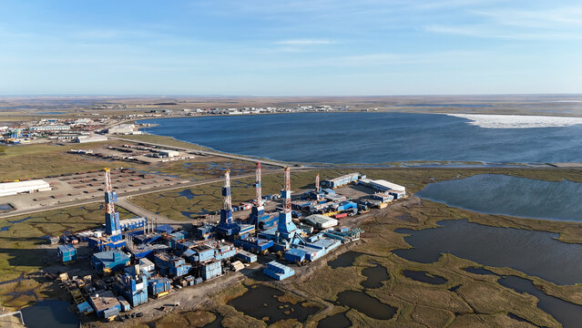 Oil drilling rigs and industrial facilities on prudhoe bay tundra beside icy bay waters, aerial view of north slope oil field and infrastructure amid arctic landscape, Alaska, US