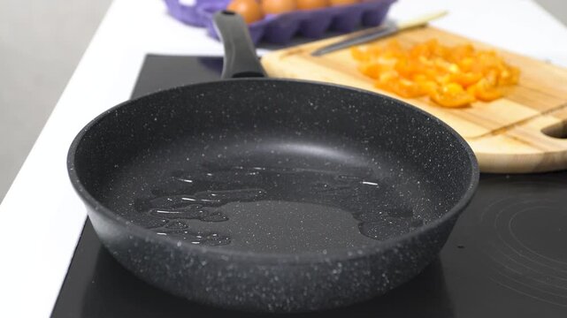A hand is using a spatula to stir oil in a frying pan at a kitchen counter while breakfast items are prepared nearby.