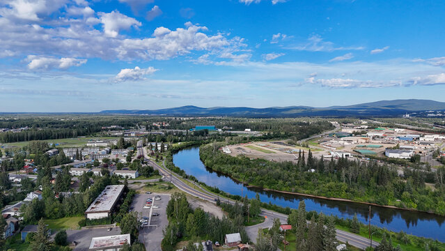 Fairbanks, alaska aerial summer view of the chena river winding through city neighborhoods, commercial areas, roads and lush forests with distant mountains under blue sky
