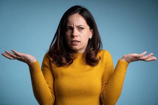Beautiful young brunnete confused woman posing isolated over blue wall background.