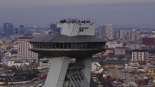 Aerial pan shows the UFO deck atop SNP Bridge in Bratislava, Slovakia. The camera moves slowly, visitors walk on the terrace, and metallic tones stand out.