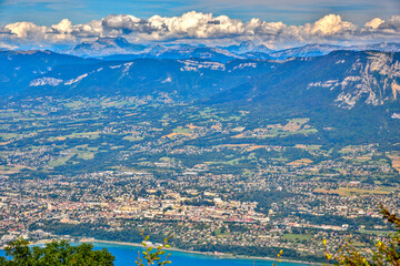 Obraz premium Aerial view from Dent du Chat over Lac du Bourget and Aix-les-Bains with mountain ranges under a clear summer sky.