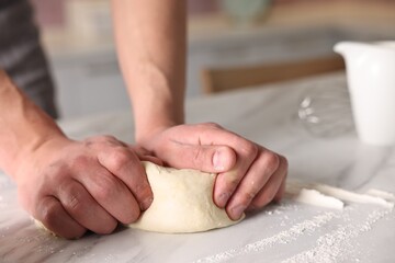 Fototapeta premium Man kneading dough at white table indoors, closeup. Space for text