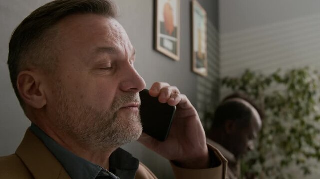 Close up shot of middle aged man having serious phone call conversation in waiting area of modern bank