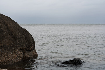 Large dark boulder in the water on the coast of the Gulf of Finland in Estonia. Minimalist sea landscape with a calm horizon under a cloudy sky in early April. © Alexander Korotkov