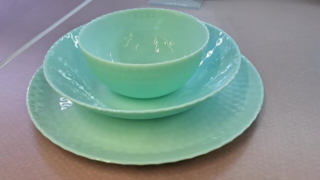 Set of mint green dinnerware featuring bowl, dessert plate, dinner plate on neutral surface. Modern table setting and kitchenware. Elegant turquoise glass tableware set with unique honeycomb texture