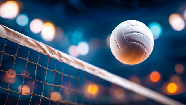 A volleyball is suspended between the net and stadium lights.