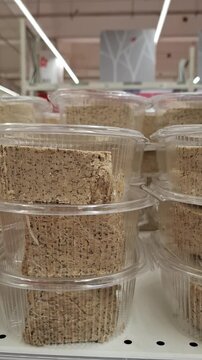 Sunflower halva with poppy seeds packed in clear plastic containers on a supermarket shelf. The stack of traditional oriental sweets shows a crumbly texture and greyish tone of the dessert