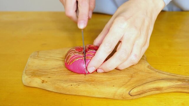 Female hands slicing pink mochi with chocolate glaze, revealing a creamy layer and berry filling flowing from the center. Symbolizes ASMR food, molten core reveal, and sensory dessert interaction.