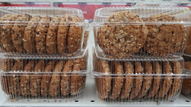 Oatmeal cookies with various seeds in transparent plastic packaging on retail shelf. Healthy snacks with visible grains, sunflowers, and sesame seeds. Multigrain biscuits