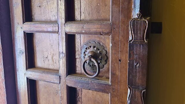 A close-up of a rustic wooden door at Kanak Vrindavan Mahal. It features a decorative metal ring handle and aged paneling, showcasing the historic architectural details of Jaipur.