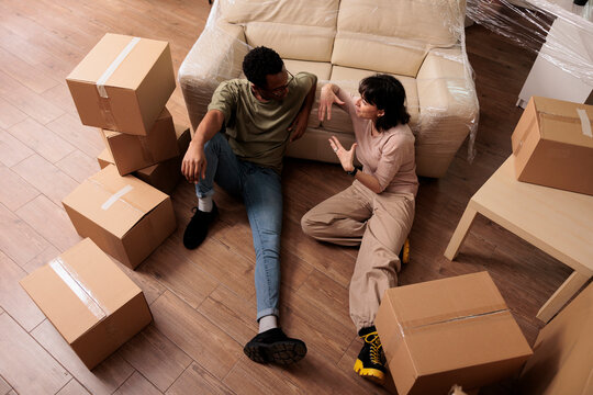 Diverse husband and wife dreaming about new household property, thinking about family beginnings. Taking break after moving in apartment flat bought on mortgage loan. Top view of.