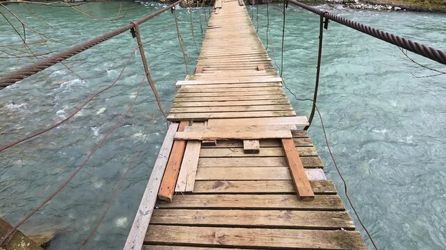 First-person perspective walking on old wooden suspension bridge over a mountain river in a forest during autumn