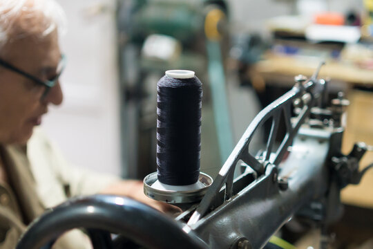 Latino upholsterer works on a backpack repair with a sewing machine and thread spool