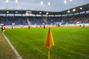 Yellow corner flag on a green grass soccer pitch with a blurred view of a professional stadium and crowd in the background. © Dziurek