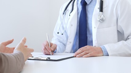 Adult aged doctor man taking notes while listening to a female patient explaining her symptoms...