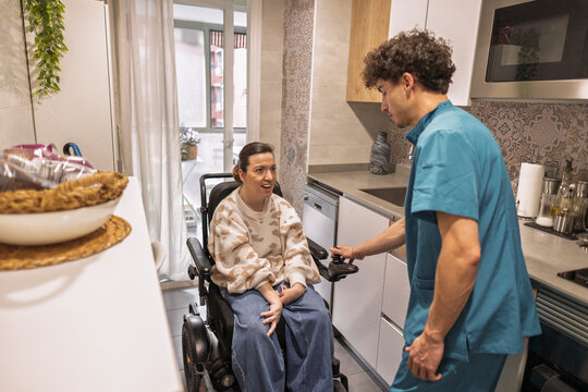 Caregiver assisting disabled woman in home kitchen