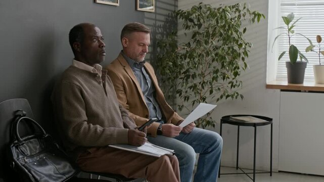 African American man expressing his confusion about young man skipping line at bank, while another man kindly reassuring him