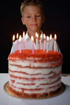 A boy looks at a birthday cake with lots of candles. Traditional rituals strengthen family bonds and create long term memories in human psychology.