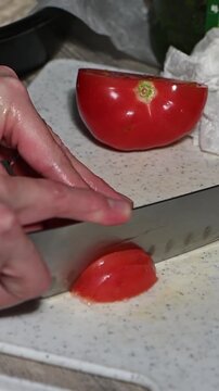 Close up of a sharp knife slicing a fresh ripe tomato on a cutting board. Juicy red pulp, seeds and smooth skin visible in high detail. Clean precise cutting motion, natural kitchen light, healthy foo
